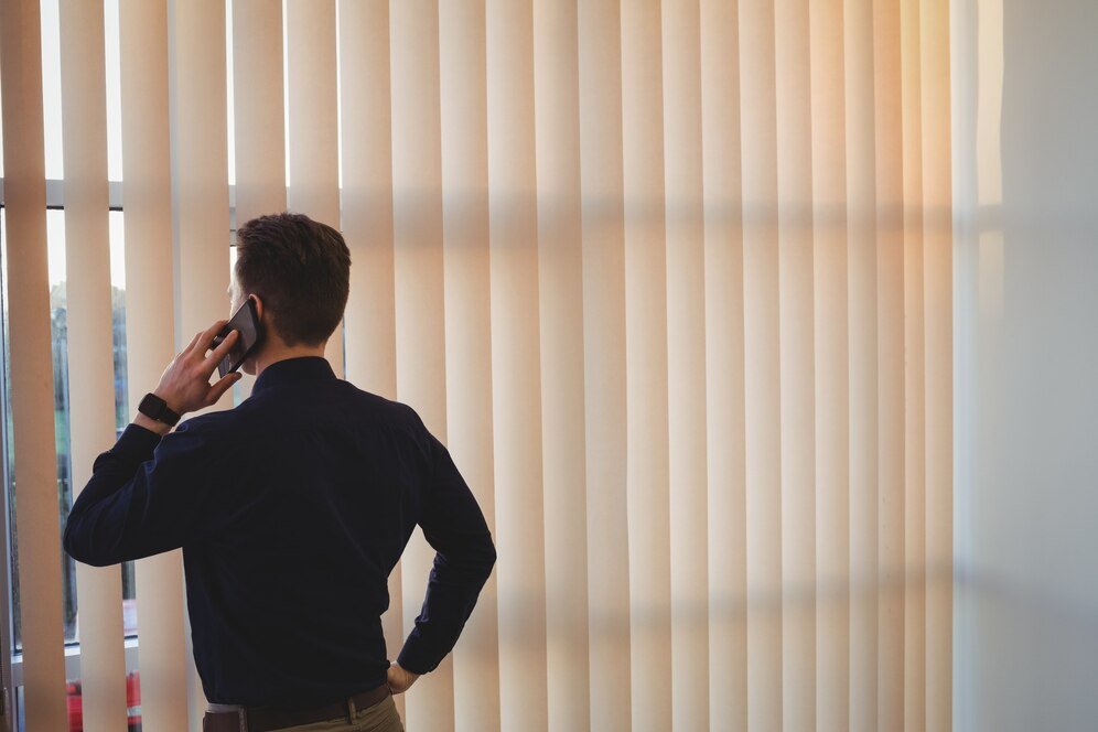 male-executive-talking-mobile-phone-near-window-blinds_107420-96247